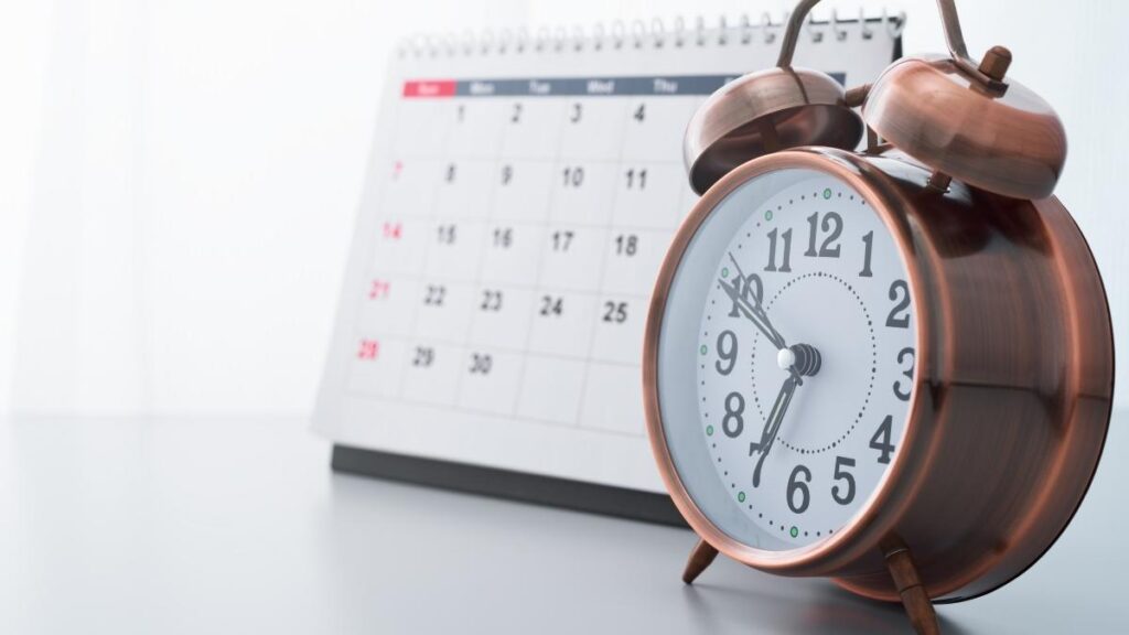 An alarm clock in front of a calendar.